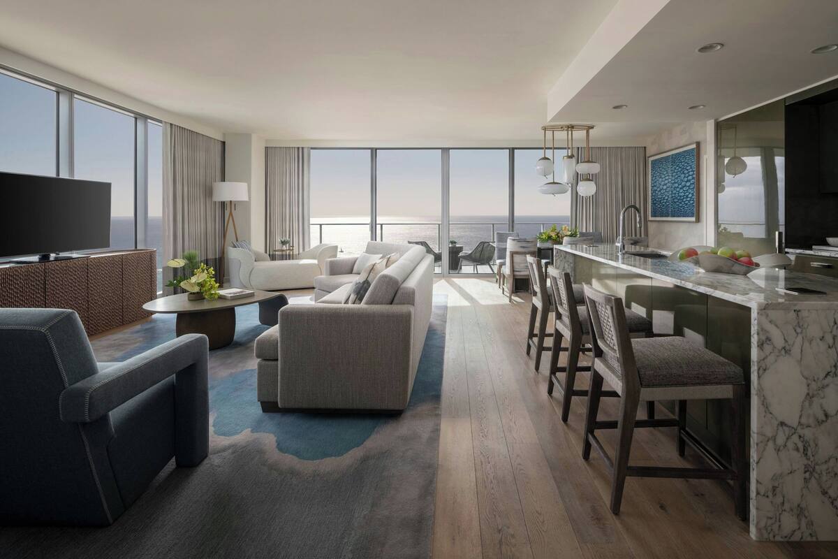 A modern hotel room with a large balcony, a dining area, and a living room.