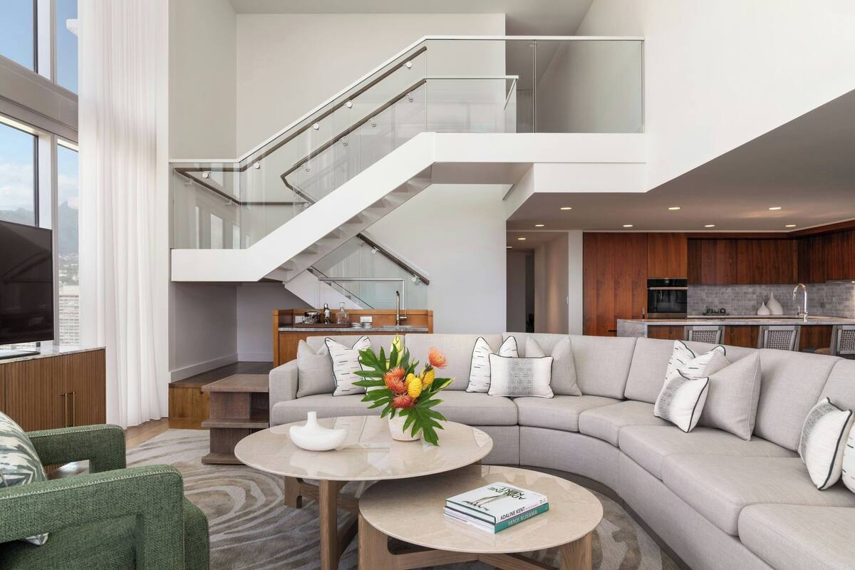 A modern living room with a sectional sofa, a coffee table, and a staircase with glass railings.