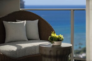 A wicker sofa with cushions and a small table with a plant, overlooking a scenic ocean view.