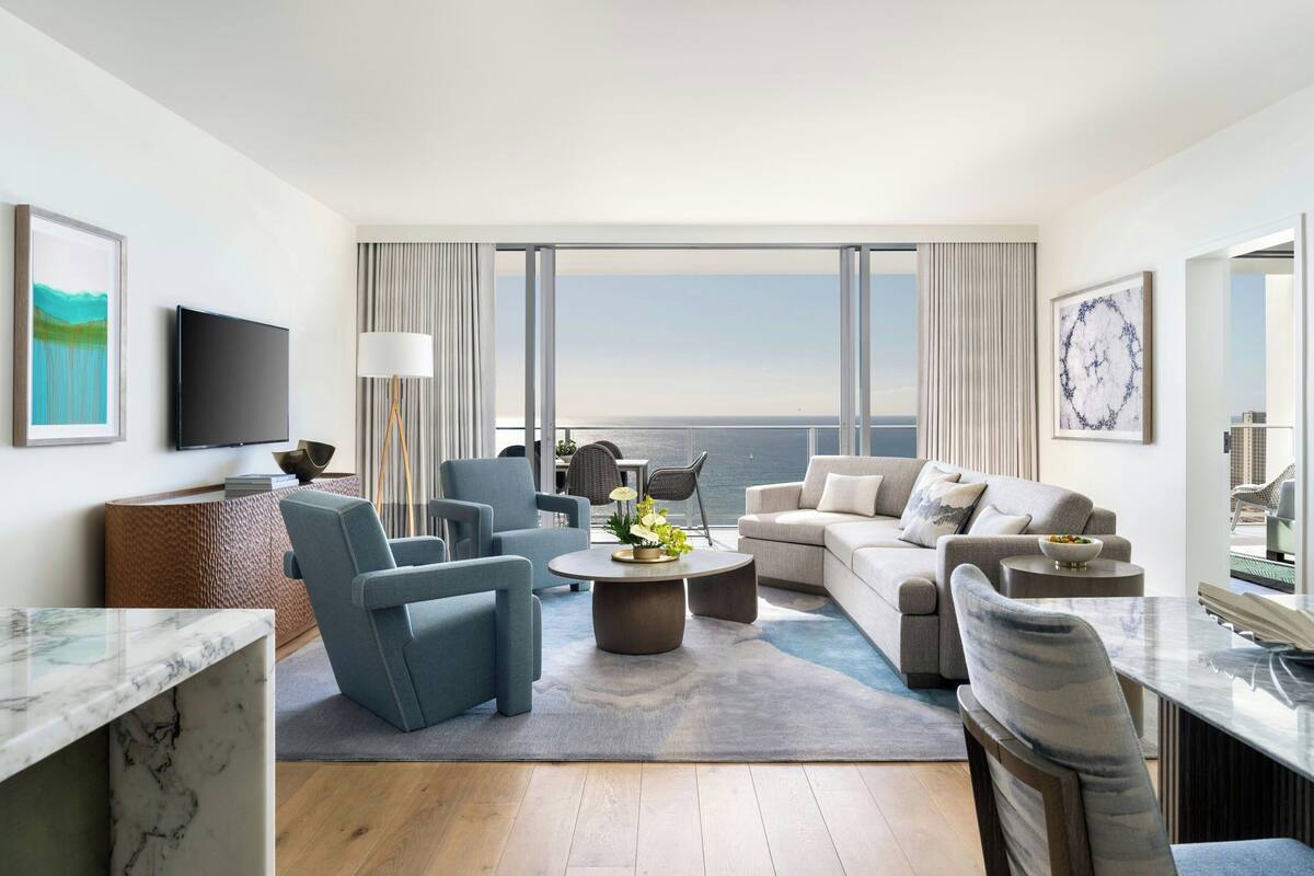 A modern living room with a large window, a flat-screen TV, a sofa, a coffee table, and a dining area.