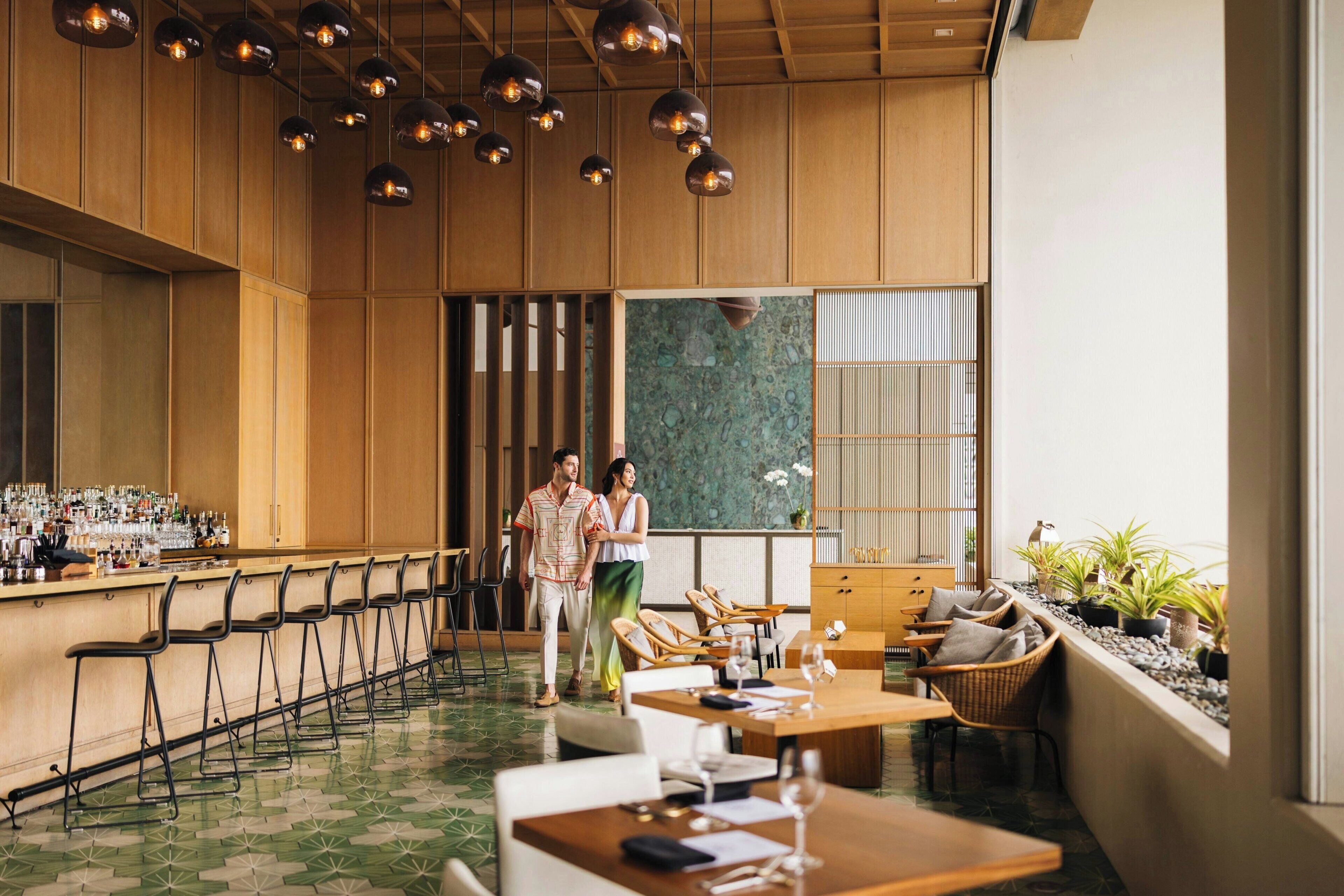 A modern bar area with wooden paneling, hanging pendant lights, and a bar counter with stools.