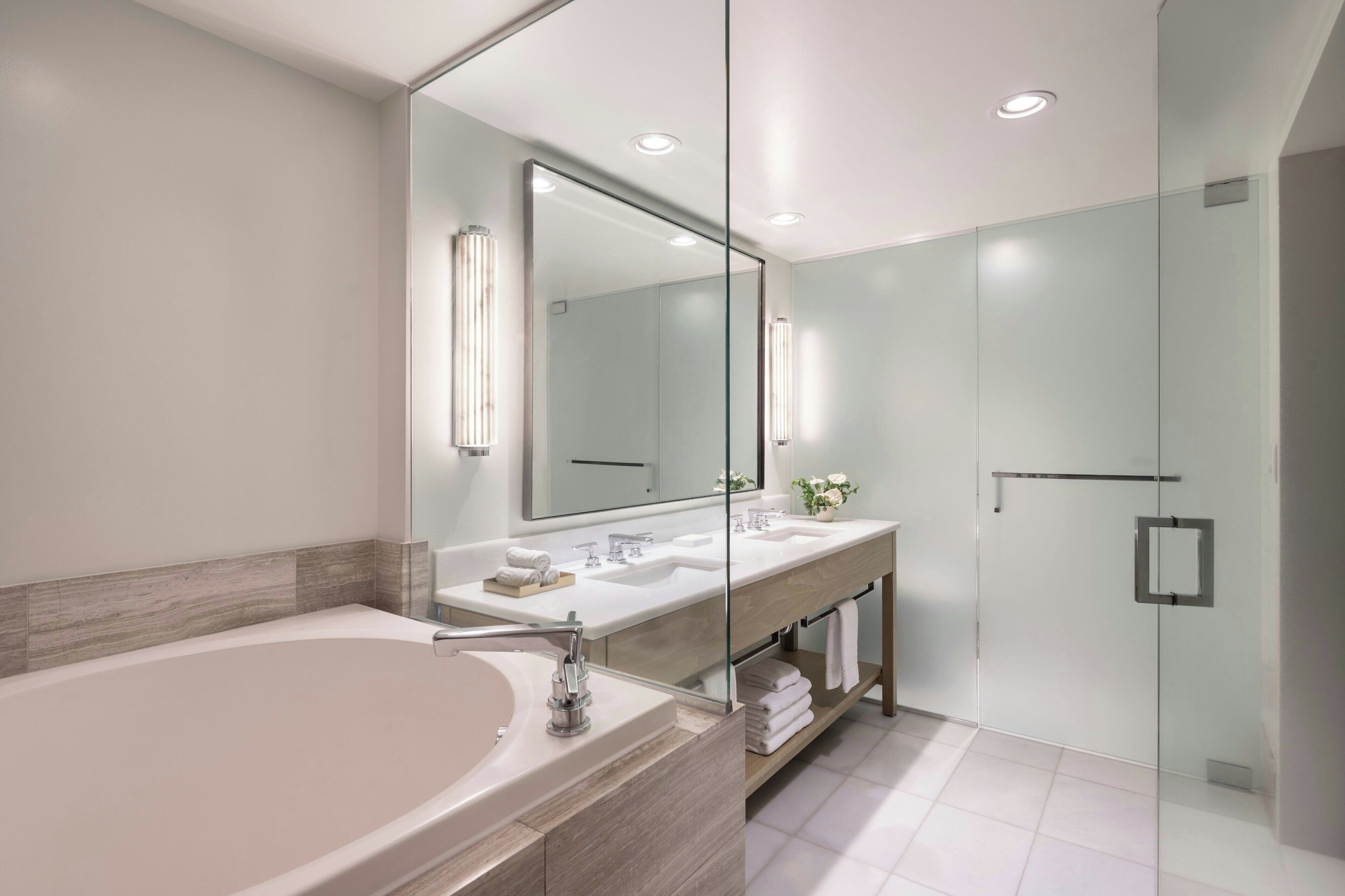Ein modernes Badezimmer mit einer großen Badewanne, zwei Waschbecken, einer Duschkabine aus Glas und einem großen Spiegel.
