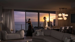 A modern living room with a large sofa, a dining area, and a view of the sunset through floor-to-ceiling windows. - The Ritz-Carlton Residences, Waikiki Beach (Honolulu)