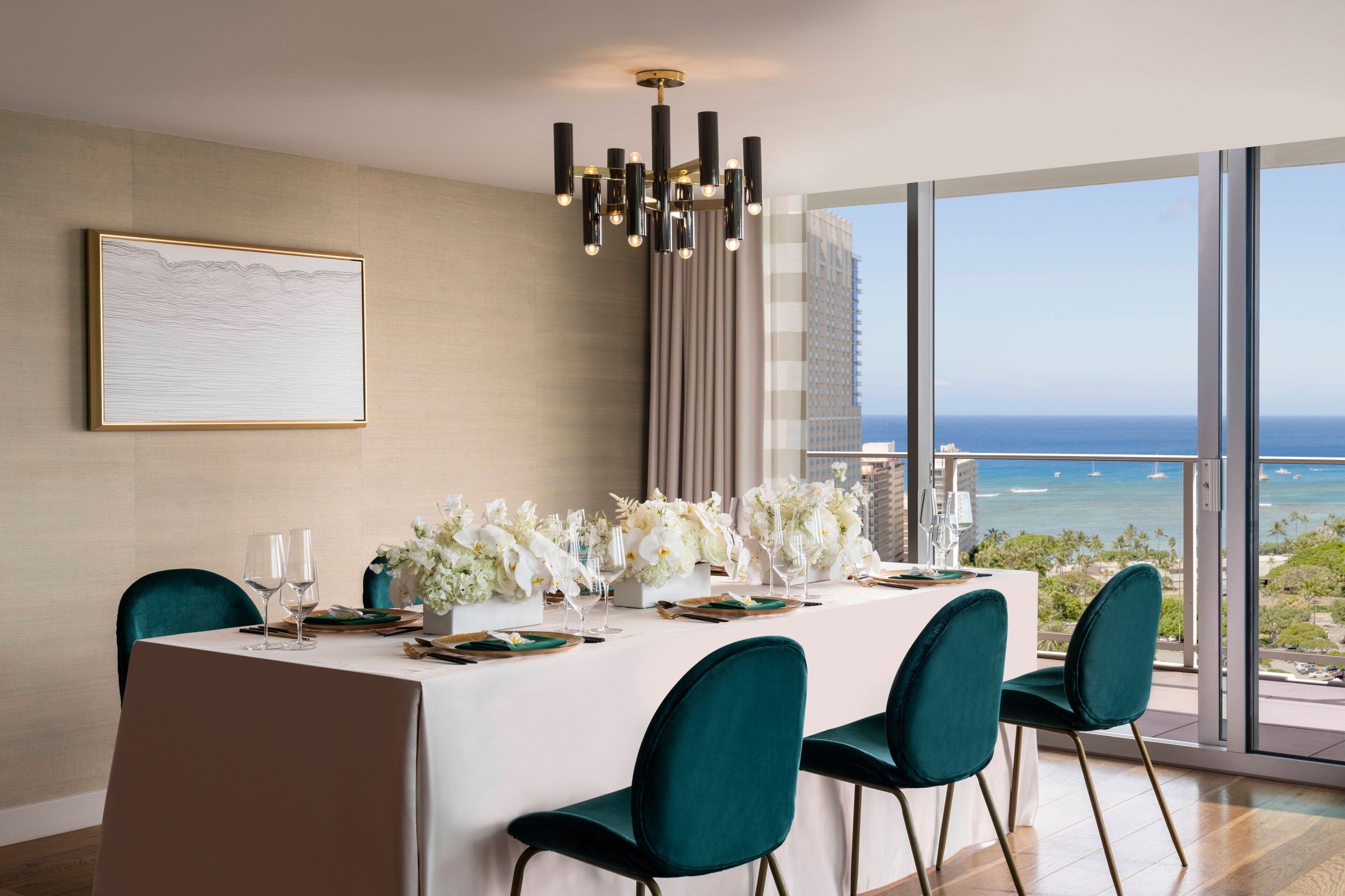 A dining area with a table set for four, a chandelier, and a view of the ocean.