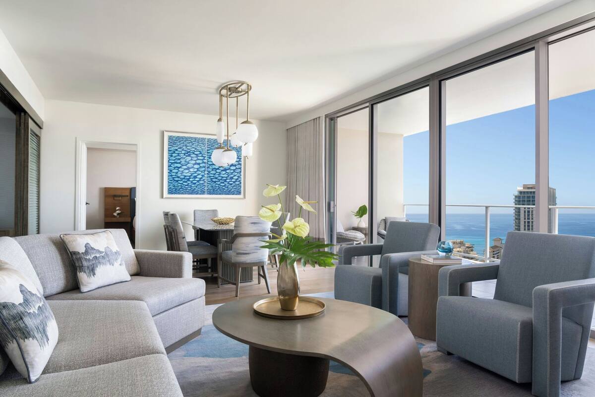 A modern hotel room with a large balcony, a dining area, and a view of the city skyline.