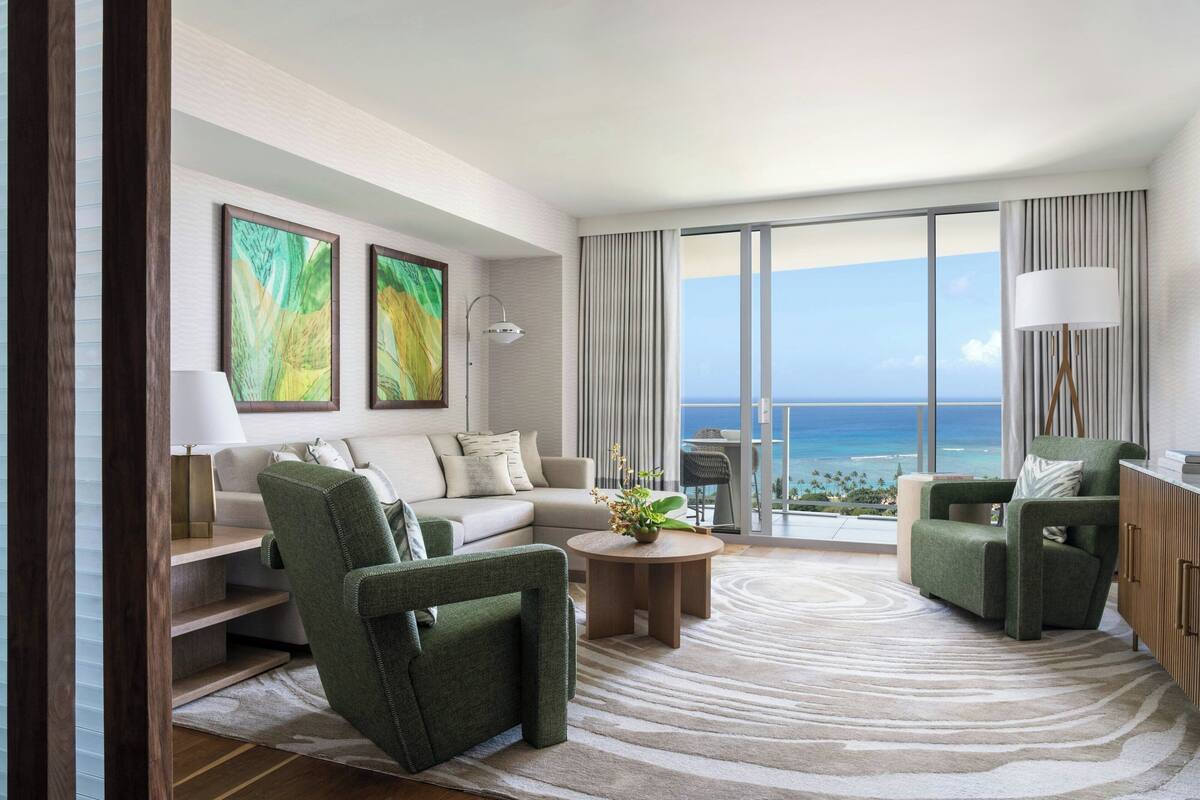 A modern living room with a sofa, two armchairs, a coffee table, and a view of the ocean.