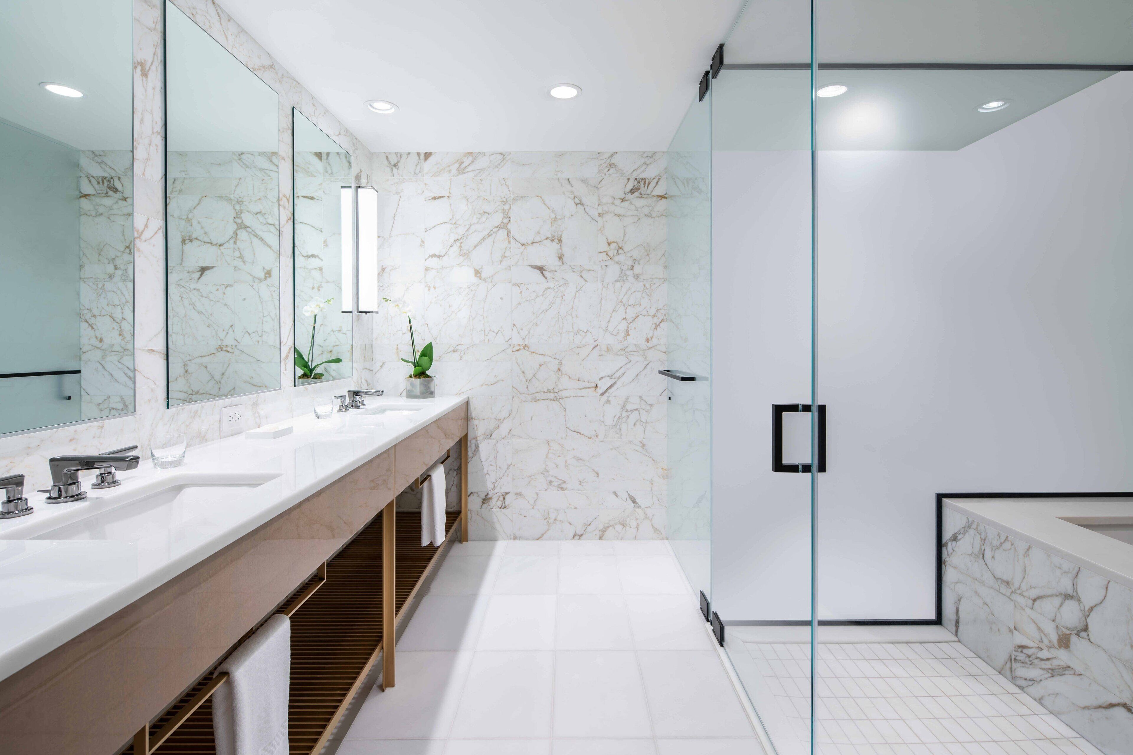 A modern bathroom with marble walls, a glass shower enclosure, and a vanity with dual sinks.