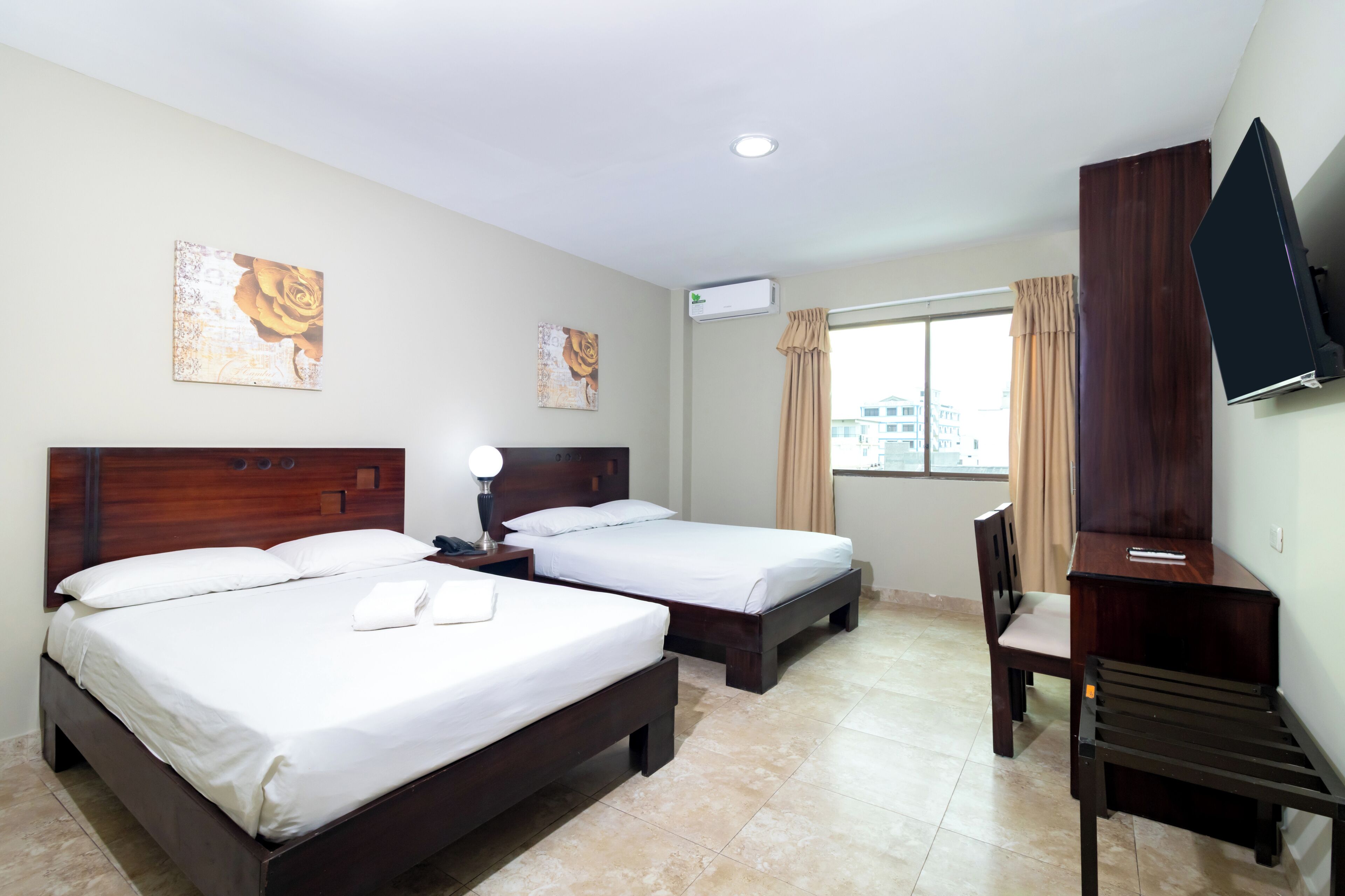 A hotel room with two beds, a desk, a chair, a TV, and artwork on the walls.