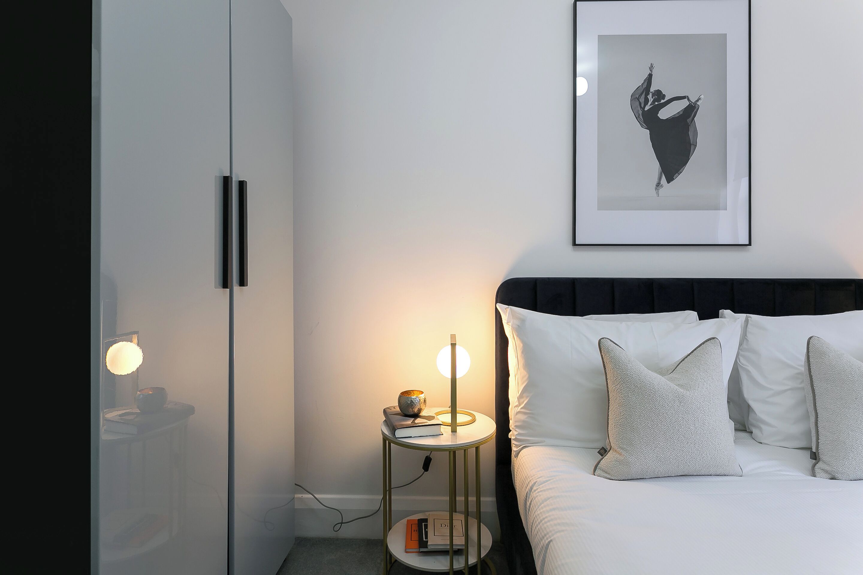 A bedroom with a bed, bedside table, lamp, and a framed picture on the wall.