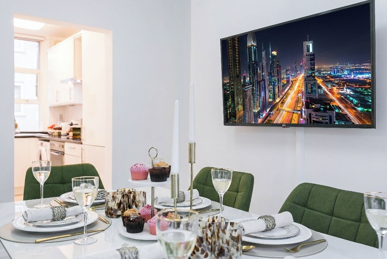 A dining area with a cityscape view, green upholstered chairs, and a table set with plates, glasses, and cupcakes.