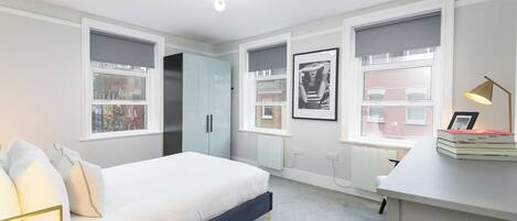 A modern bedroom with a bed, bedside table, and a desk with a lamp.