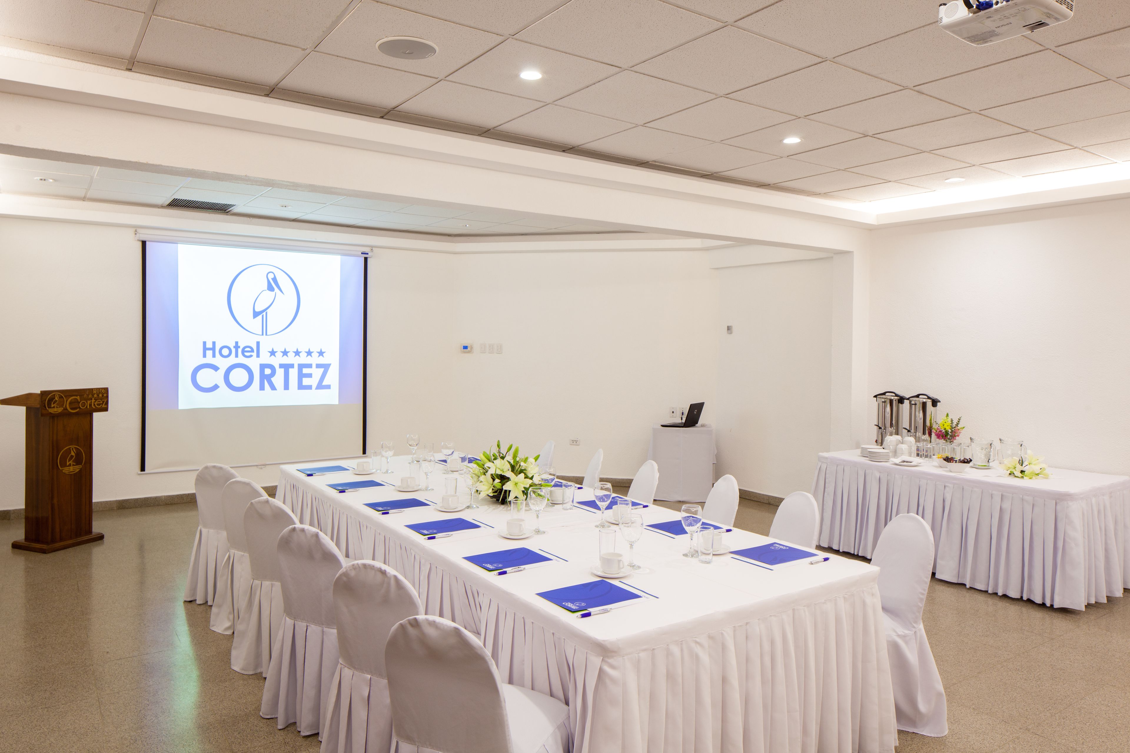 A conference room with a long table, white chairs, and a podium.