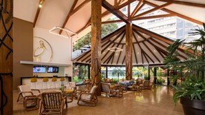 Un hall d’entrée spacieux avec de hauts plafonds, des poutres en bois et un grand espace salon équipé de fauteuils en osier.