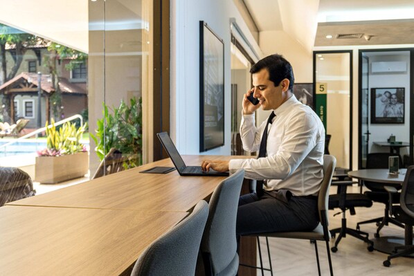 A man sitting at a wooden table with a laptop, talking on a phone.