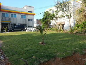 Un césped con un árbol pequeño, sillas blancas y una furgoneta estacionada.