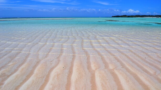 Une plage à l’eau turquoise et limpide, avec un sol sablonneux où l’on peut distinguer de légères ondulations.