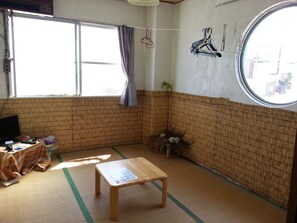 Una habitación con suelo de tatami, una mesa de madera, un televisor y una ventana con cortinas.