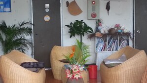Un espace d’accueil avec des fauteuils en osier, une plante au centre, un gobelet rouge et une porte dotée d’un panneau de sécurité.