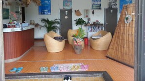 Un espace d'accueil comprenant un comptoir, deux fauteuils en osier, une plante en pot et un présentoir mural.