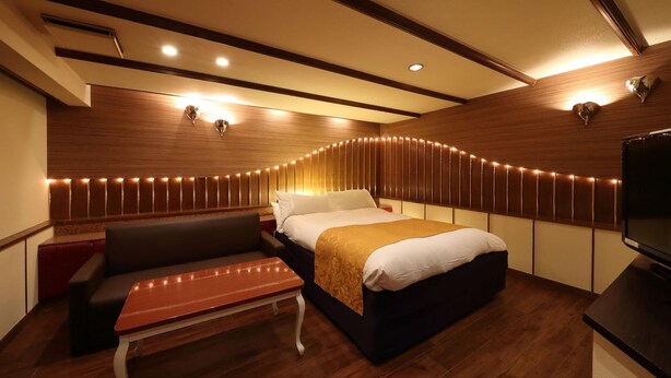 Une chambre d’hôtel moderne équipée d’un lit, d’un banc, d’une télévision et d’une tête de lit en bois avec des lampes.