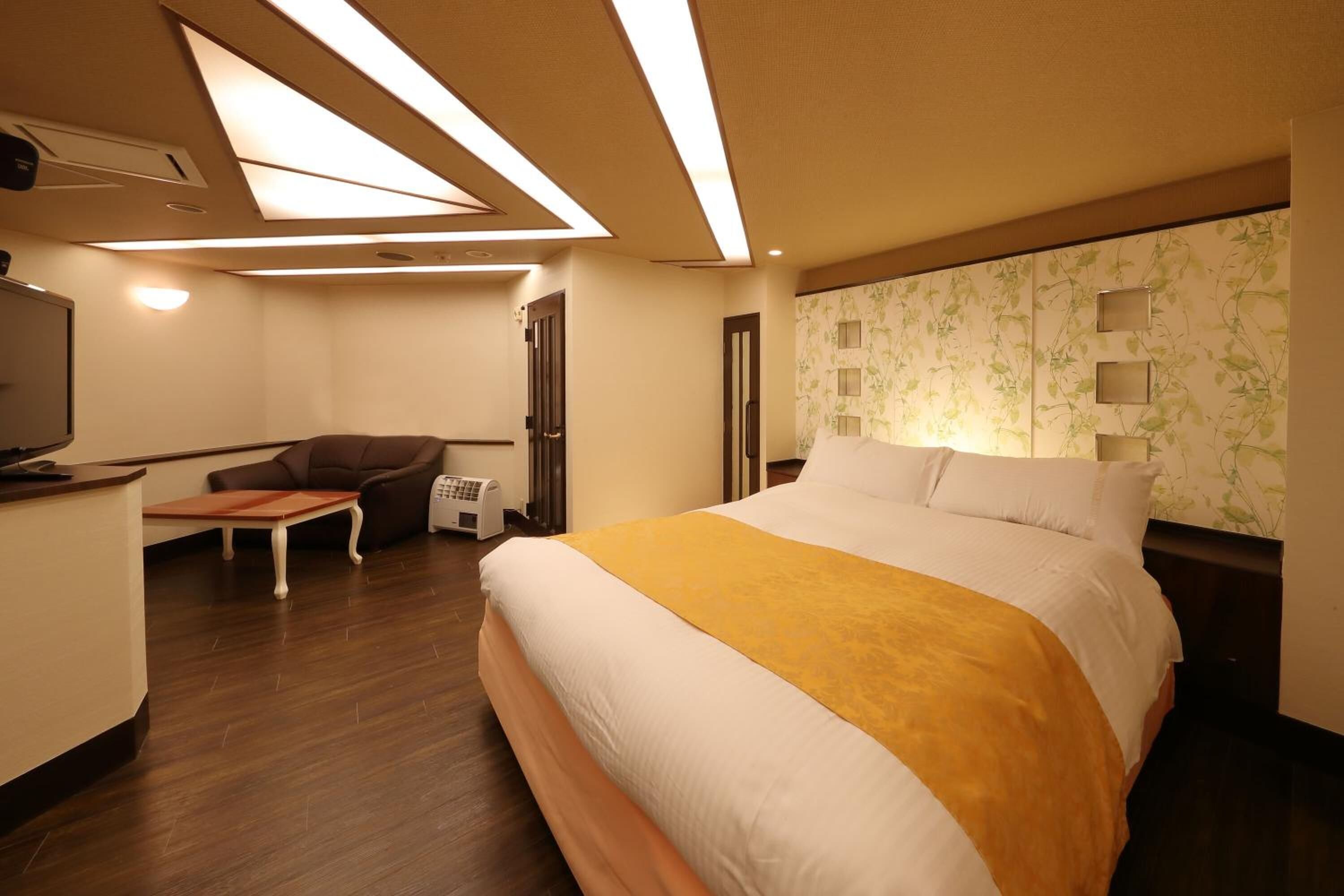 Habitación de hotel con cama, escritorio, silla, televisor y pared con estampado floral.
