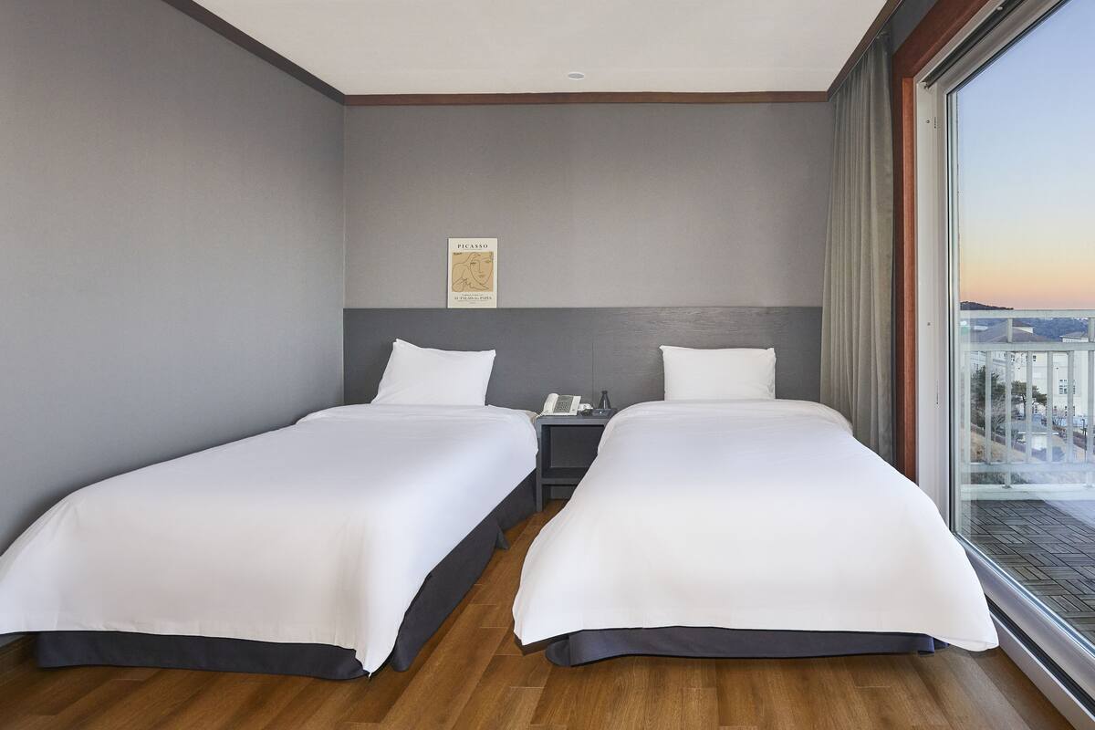 A hotel room with two beds, a nightstand, a telephone, and a large window with a city view.