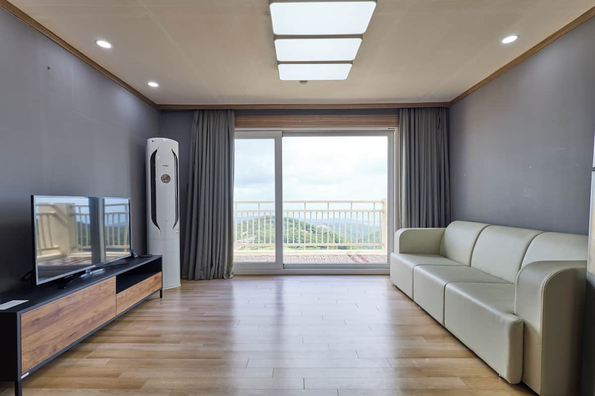 A modern living room with a flat-screen TV, a sofa, and a sliding glass door leading to a balcony.
