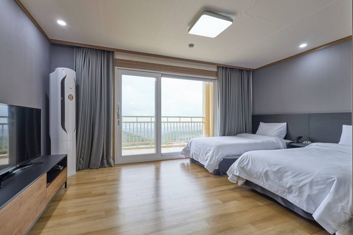 A hotel room with two beds, a TV, a balcony with curtains, and a ceiling light.