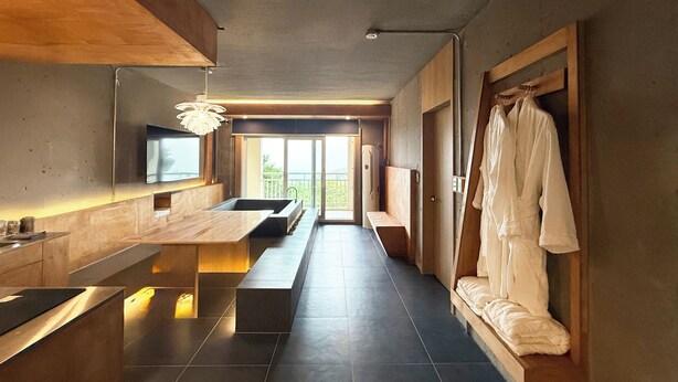 A modern bathroom with a large sink, bench, and a robe hanging on a wooden rack. - The Mauna Ocean Resort (Gyeongju)