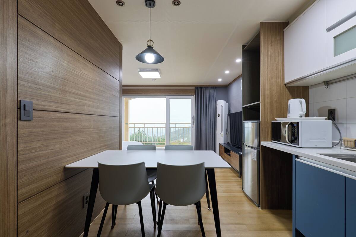 A modern kitchen with a dining area, wooden cabinetry, a white countertop, and a view to the outside.