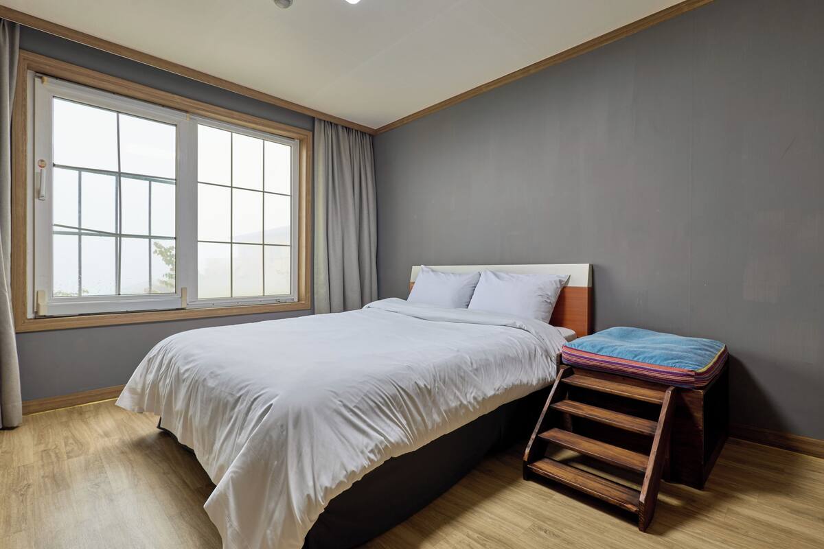 A bedroom with a bed, a window, and a wooden ladder.