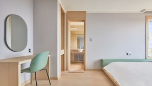 A modern bedroom with a wooden desk, a green chair, a bed with white bedding, and a bathroom visible through an open door. - The Mauna Ocean Resort (Gyeongju)