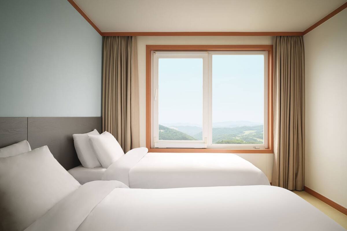 A hotel room with two beds, a large window, and curtains.