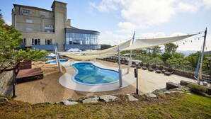 A pool area with a curved design, lounge chairs, and a building with large windows in the background. - The Mauna Ocean Resort (Gyeongju)