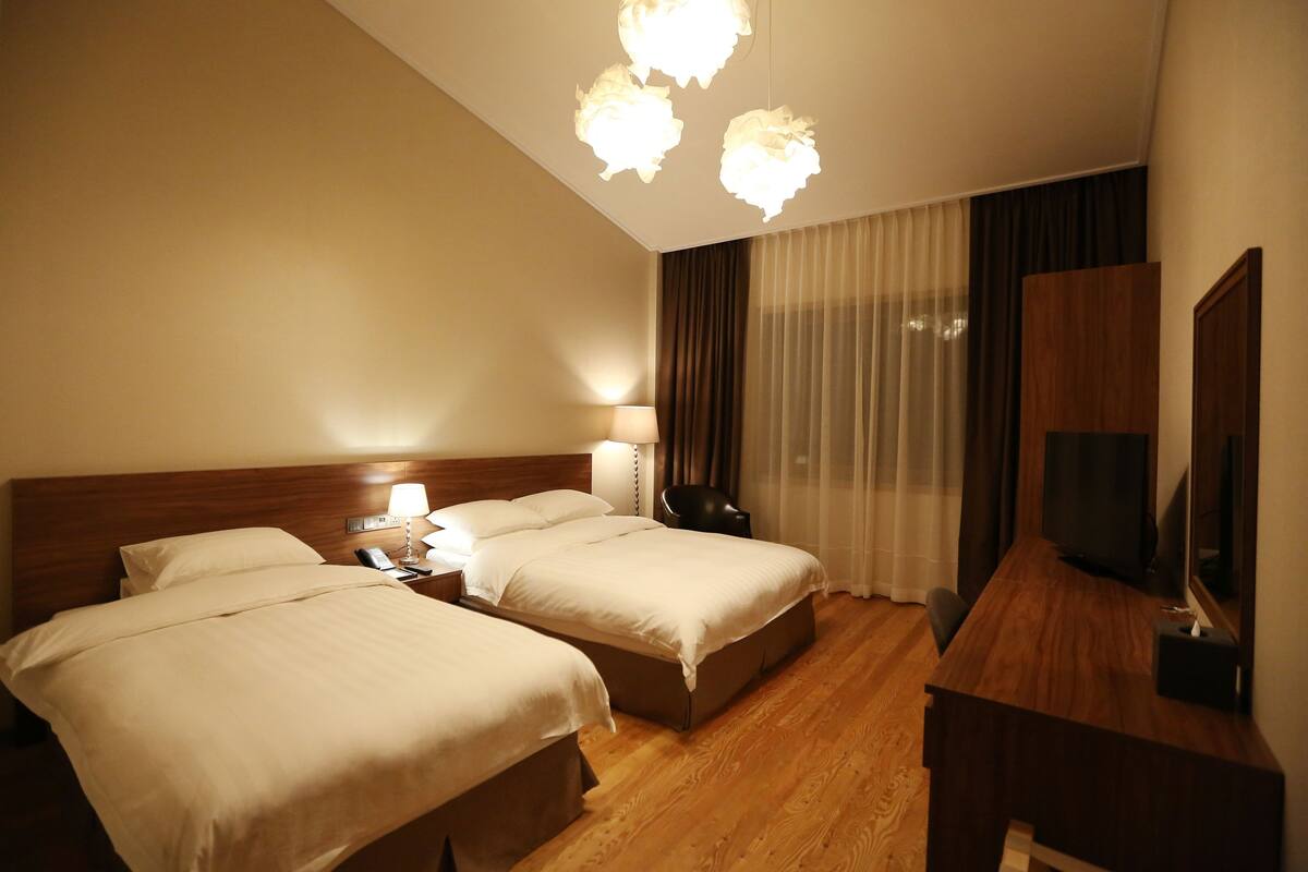 A hotel room with two beds, a desk, a television, and a lamp.