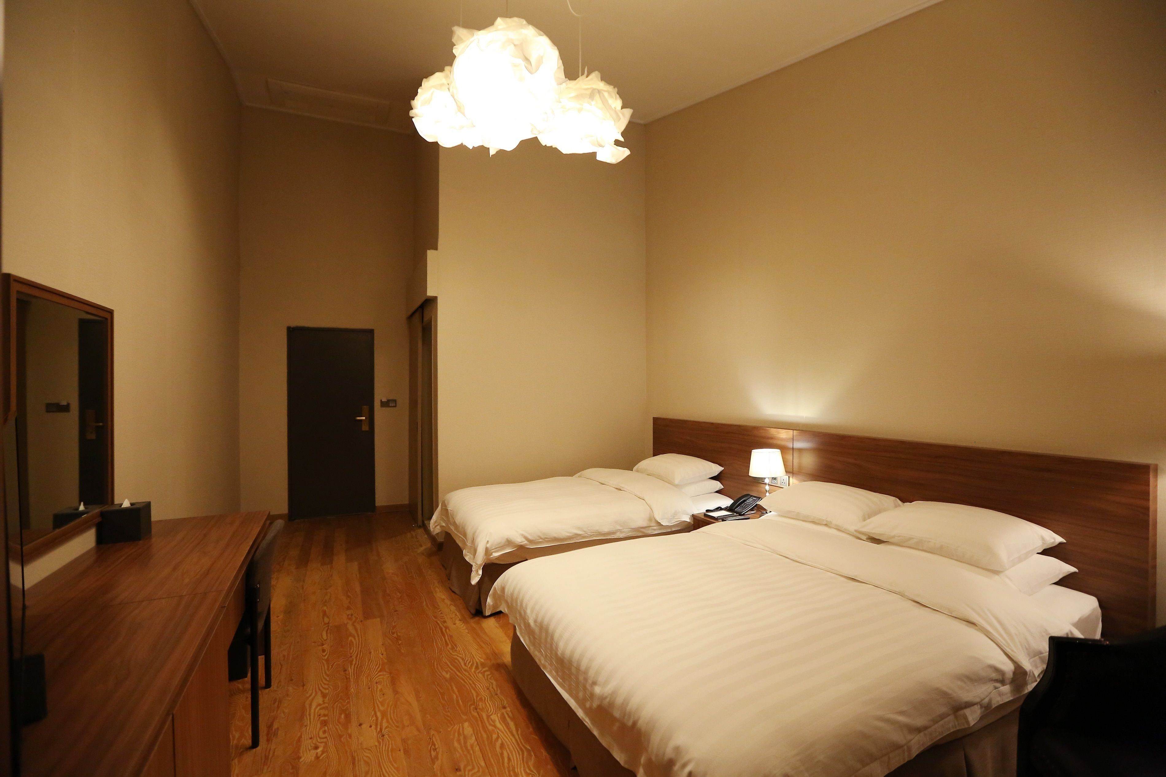 A hotel room with two beds, a wooden bench, a mirror, and a ceiling light fixture.