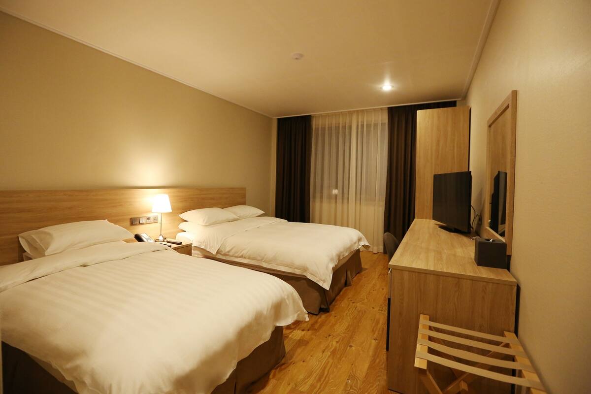 A hotel room with two beds, a desk, a chair, a TV, and a window with curtains.