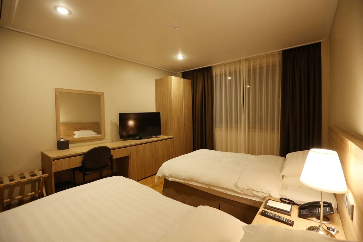A hotel room with two beds, a desk with a chair, a TV, a bedside lamp, and a telephone.
