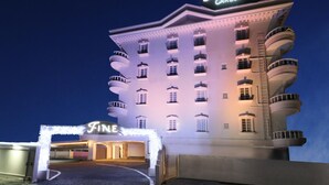 Un hôtel reconnaissable à son panneau bien visible indiquant « Hotel Fine Garden », doté de nombreux balcons et d’une entrée bien éclairée.