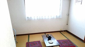 A small room with tatami mats, a table with a black kettle, and a window with blinds. - Share House Miyabi (Hakodate)
