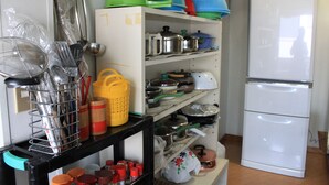A kitchen with shelves holding pots, pans, and utensils. There is a white refrigerator and a black countertop with a sink. - Share House Miyabi (Hakodate)