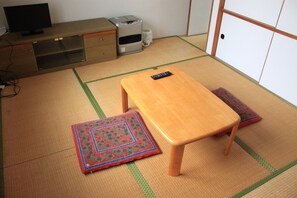 A tatami mat room with a wooden table and two matching cushions, a television on a cabinet, and a heater. - Share House Miyabi (Hakodate)