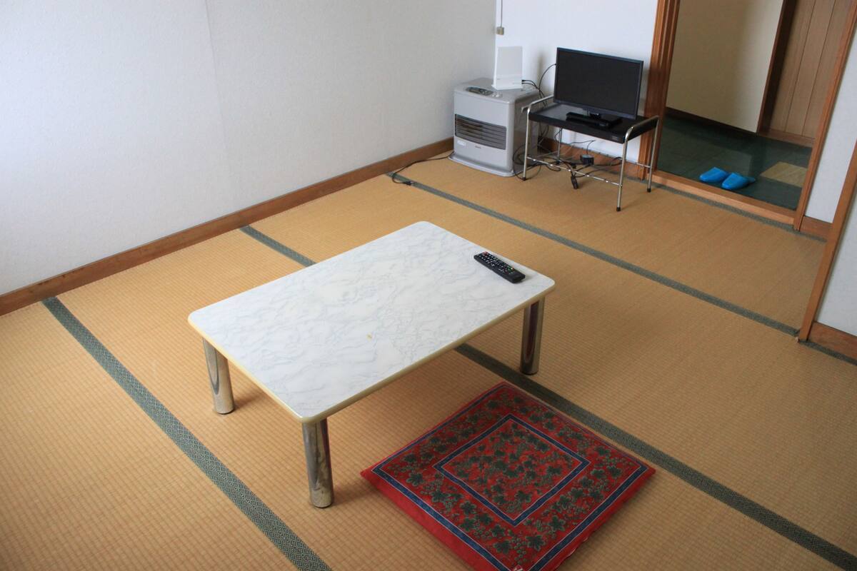 Una habitación con suelo de tatami, una mesa baja, un control remoto y un televisor sobre un mueble.