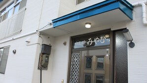 A building with a blue awning, a decorative door with a lattice pattern, and a sign with Japanese characters. - Share House Miyabi (Hakodate)