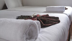 Cama doble con sábanas blancas y una toalla enrollada a la izquierda.