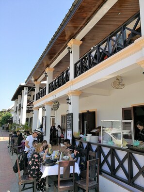 An outdoor cafe with tables and chairs, a wooden ceiling, and a signboard. - Sokxai Residence (Luang Prabang)