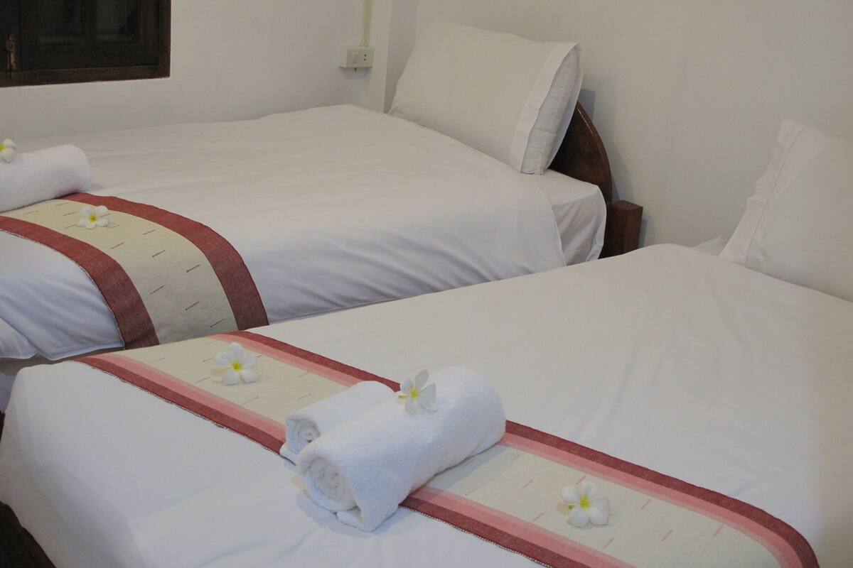 Two hotel beds with white linens and red trim, each with a rolled white towel and a white flower.