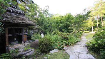Un jardín japonés tradicional con un sendero de piedra, construcciones de madera y abundante vegetación.