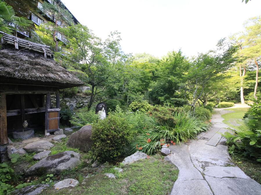Un jardín japonés tradicional con un sendero de piedra, construcciones de madera y abundante vegetación.
