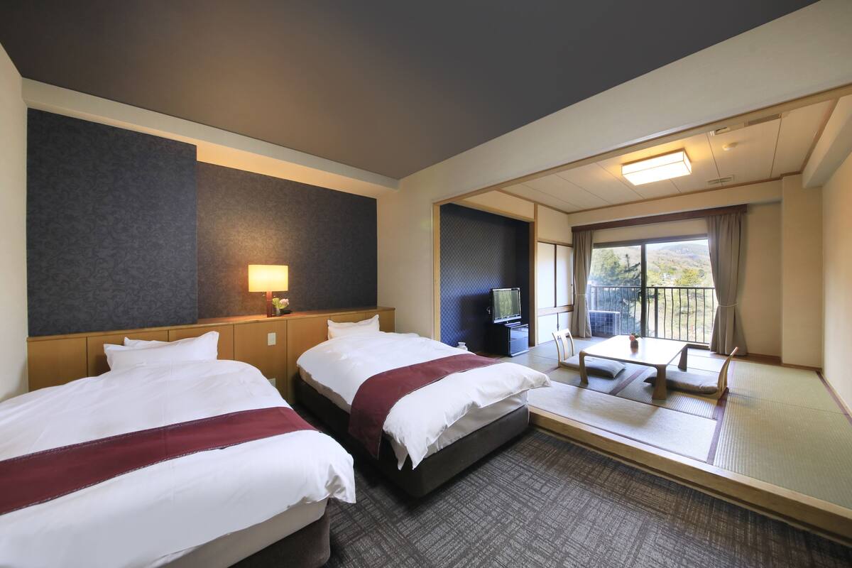 A hotel room with two beds, a TV, a desk with a chair, and a balcony with a view.